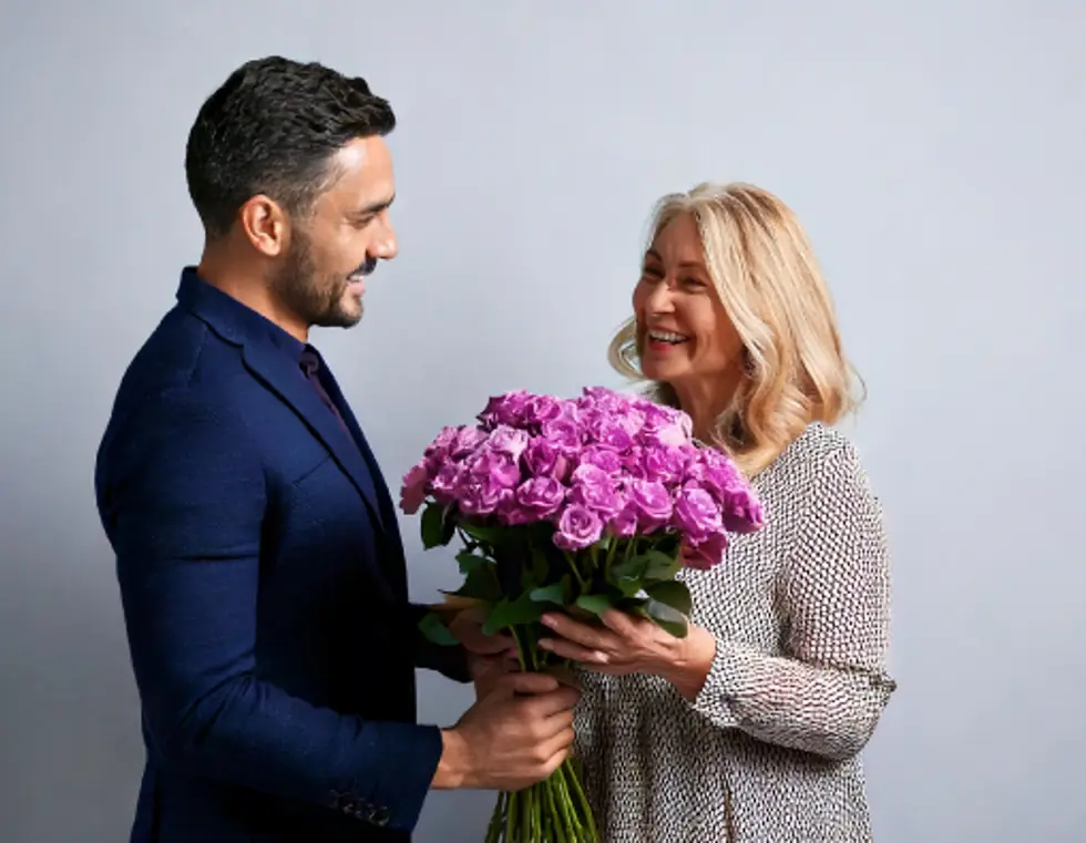 A man giving a bunch of purple roses to his mother